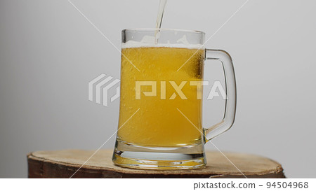 Beer is poured into a beer glass with a handle, a lot of bubbles and foam. Beer is poured into a beer glass with a handle, a lot of bubbles and foam. 94504968