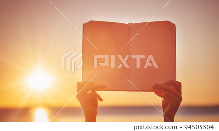 Human hands holding empty textbook outdoors on the sunset Human hands holding empty textbook outdoors on the sunset 94505304
