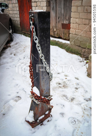 Parking lot post with steel chains used to close the parking lot standing in snow covered yard outdoors 94505598