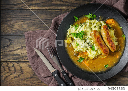 Dutch stamppot of potatoes, kale and sausages with gravy on plate above 94505863