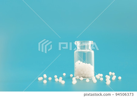 Close-up image of homeopathic globules in glass bottle on blue background. Homeopathy pharmacy, herbal, natural medicine, alternative homeopathy medicine, healthcare. Free space, copy space. 94506373
