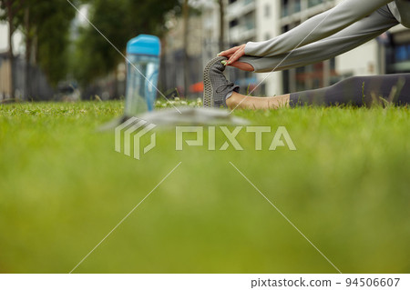 Close up of woman doing stretching exercise on green grass at city park Close up of woman doing stretching exercise on green grass at city park 94506607