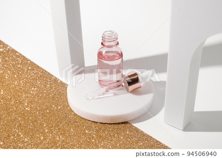 Pink glass bottle of cosmetic liquid transparent gel on white background with golden sheet. Dropper bottle, hyaluronic acid, oil, serum, skin care product. 94506940