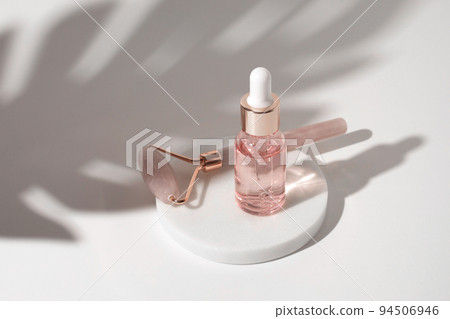 Massage quartz roller and pink glass bottle of cosmetic liquid transparent gel on white background. Dropper bottle, hyaluronic acid, oil, serum. Facial massage and relaxation. Gua Sha massage tools. 94506946