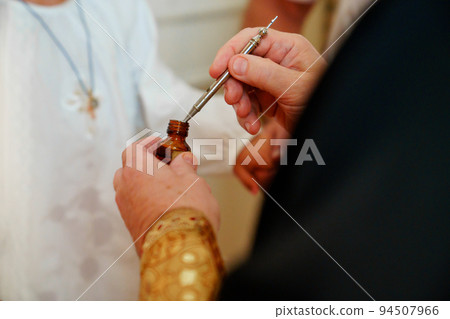 the priest holds the myrrh oil for the baptism of a boy in a baptismal shirt.  94507966