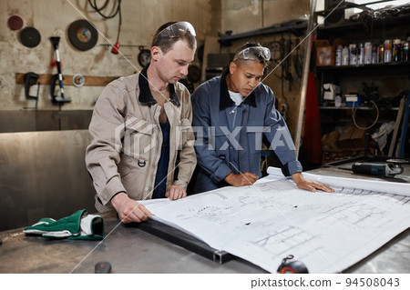 Two Workers Looking At Plans In Factory Two Workers Looking At Plans In Factory 94508043