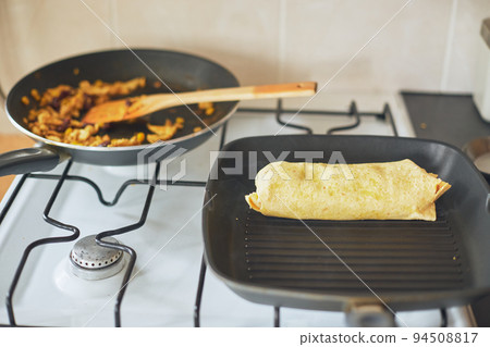 Cooking burrito, Mexican food at home. Grilled wheat tortilla stuffed with cheese, chicken, beans, corn, lettuce, tomato and sauce Cooking burrito, Mexican food at home. Grilled wheat tortilla stuffed with cheese, chicken, beans, corn, lettuce, tomato and sauce 94508817