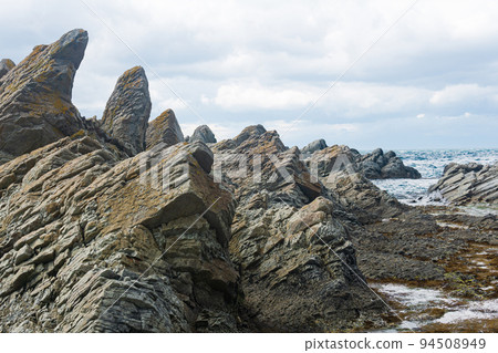 rocks formed by solidified lava against a blurred coastal seascape 94508949