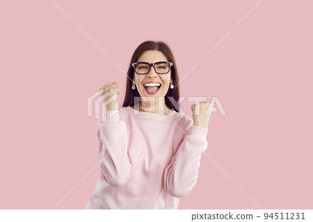Happy excited woman rejoices success, clenched fists and triumphantly exclaims on pink background. 94511231