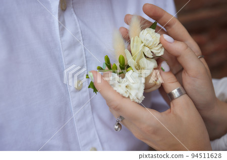 The hands of the newlyweds with gold rings close-up against the background of a plaid jacket with a boutonniere. The hands of the newlyweds with gold rings close-up against the background of a plaid jacket with a boutonniere. 94511628