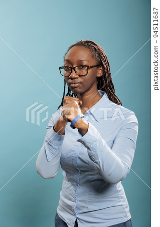 Serious and brave woman getting in ready position for boxing while clenching fists with strength on blue background. Defensive young adult person in self defense pose when encountering a life threat. Serious and brave woman getting in ready position for boxing while clenching fists with strength on blue background. Defensive young adult person in self defense pose when encountering a life threat. 94511687