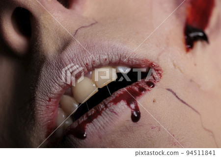 Apocalyptic zombie with bloody lips and teeth, showing wounded mouth with blood on camera. Scary evil brain eating monster having scars and wounds, dirty spooky scratches. Close up. 94511841