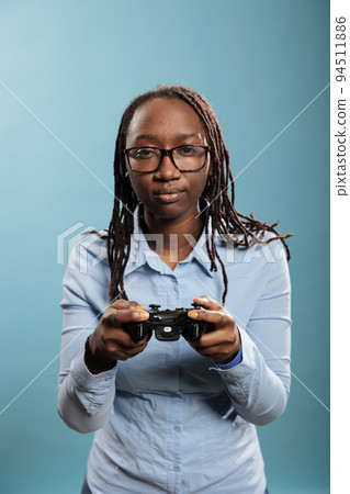 Smiling fun woman playing online videogames on gaming console with controller on blue background. Young adult person enjoying leisure time by playing games with gaming gamepad Smiling fun woman playing online videogames on gaming console with controller on blue background. Young adult person enjoying leisure time by playing games with gaming gamepad 94511886