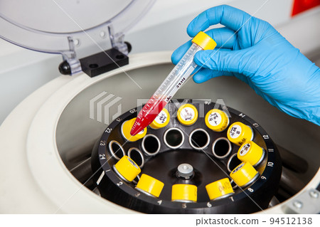 Scientist inserting a tube with a blood sample in a laboratory centrifuge. Blood test 94512138