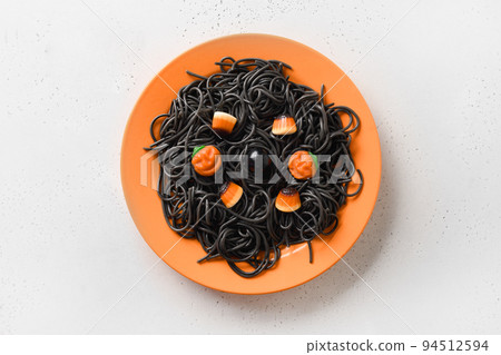 Halloween Italian black pasta decorated funny spiders in orange plate on white. 94512594