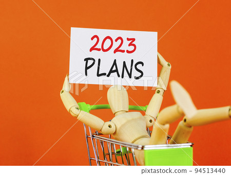 2023 Plans symbol. White paper with words 2023 Plans, human model in shopcart. Beautiful orange table orange background. Business and 2023 plans concept. Copy space. 2023 Plans symbol. White paper with words 2023 Plans, human model in shopcart. Beautiful orange table orange background. Business and 2023 plans concept. Copy space. 94513440