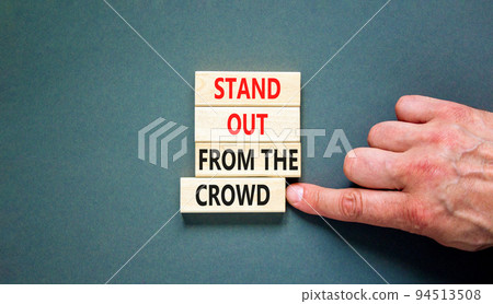 Stand out from the crowd symbol. Concept words Stand out from the crowd on wooden blocks on beautiful grey table grey background. Businessman hand. Business, stand out from the crowd concept 94513508