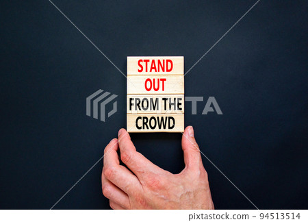 Stand out from the crowd symbol. Concept words Stand out from the crowd on wooden blocks on beautiful black table black background. Businessman hand. Business, stand out from the crowd concept 94513514