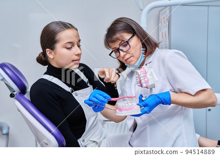 Teenage female sitting in dental chair, doctor with jaw model and toothbrush 94514889