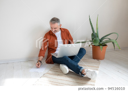 Businessman sitting on the floor in the home office and making notes 94516010