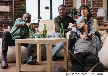 Multiethnic group of people feeling happy and playing video games on television console. Smiling friends having fun together with gaming competition and alcoholic beverage at gathering. Multiethnic group of people feeling happy and playing video games on television console. Smiling friends having fun together with gaming competition and alcoholic beverage at gathering. 94516070