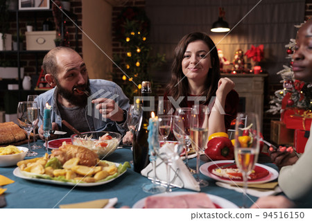 Friends celebrating christmas at festive dinner table, gathering at family home party. Man and woman eating xmas dishes in decorated beautiful place with warm candle light Friends celebrating christmas at festive dinner table, gathering at family home party. Man and woman eating xmas dishes in decorated beautiful place with warm candle light 94516150