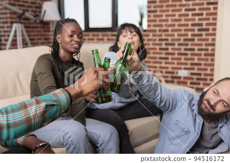 Men and women doing cheers gesture and clinking glass bottles of beer, toasting for friendship reunion at fun gathering. Cheerful people doing toast with alcoholic beverage, leisure activity. 94516172