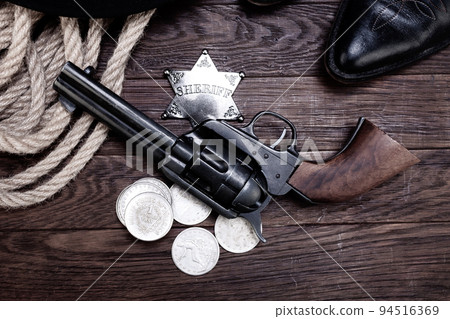 Old west law enforcement - revolver guns with sheriff badge and silver dollars with hat, rope and cowboy boots Old west law enforcement - revolver guns with sheriff badge and silver dollars with hat, rope and cowboy boots 94516369