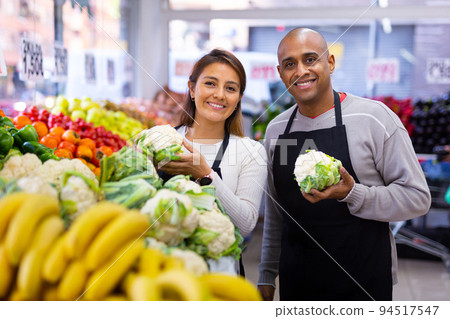 Man and woman sellers offering cauliflower in shop Man and woman sellers offering cauliflower in shop 94517547