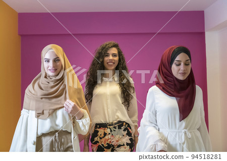 Group portrait of beautiful Muslim women two of them in a fashionable dress with hijab isolated on a pink background 94518281