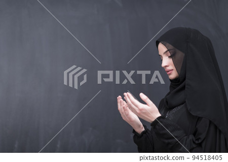 Portrait of beautiful muslim woman in fashionable dress with hijab making traditional prayer to God keeps hands in praying gesture isolated on black background 94518405