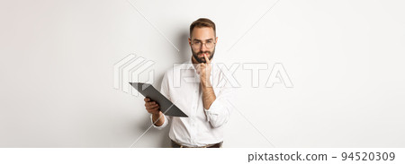 Thoughtful office employee working, holding documents on clipboard and thinking, standing over white background 94520309