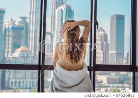 Woman wakes up in the morning in an apartment in the downtown area with a view of the skyscrapers. Life in the noise of the big city concept. Not enough sleep Woman wakes up in the morning in an apartment in the downtown area with a view of the skyscrapers. Life in the noise of the big city concept. Not enough sleep 94520938
