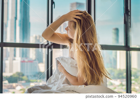 Woman wakes up in the morning in an apartment in the downtown area with a view of the skyscrapers. Life in the noise of the big city concept. Not enough sleep 94520960