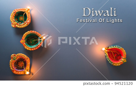 Happy Diwali - Clay Diya lamps lit during Diwali, Hindu festival of lights celebration. Colorful traditional oil lamp diya on blue background 94521120