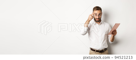 Displeased employer scolding staff while checking report on digital tablet, pointing at head and looking disappointed, standing over white background Displeased employer scolding staff while checking report on digital tablet, pointing at head and looking disappointed, standing over white background 94521213