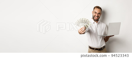 Business and e-commerce. Happy successful businessman bragging with money, working on laptop online, standing over white background 94523343
