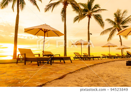 Umbrella and chair around swimming pool in hotel resort with sunrise in morning 94523849