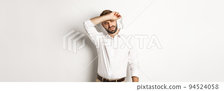 Tired office worker take-off glasses, wiping sweat off forehead with his arm, standing drained against white background 94524058