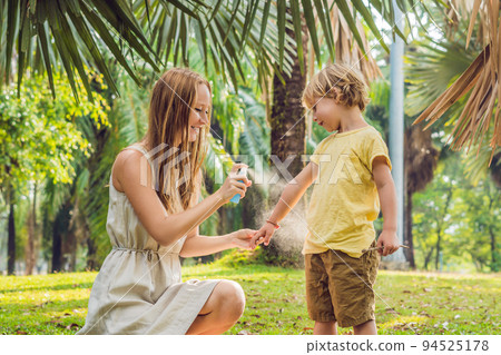 Mom and son use mosquito spray.Spraying insect repellent on skin outdoor Mom and son use mosquito spray.Spraying insect repellent on skin outdoor 94525178