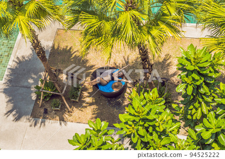 Girl in sun loungers among palm trees near the swimming pool 94525222
