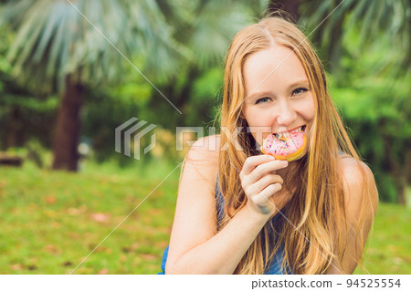 portrait of a young woman eating a donut against a plant background 94525554