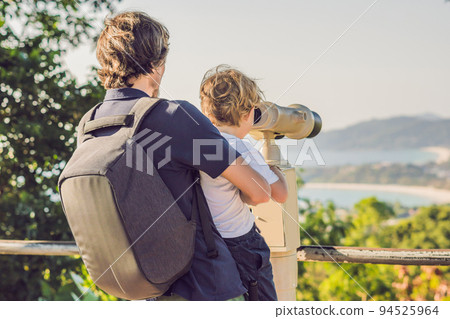 Father and son are looking at Coin-operated binoculars at the sea 94525964