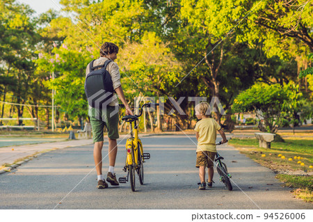 Happy family is riding bikes outdoors and smiling. Father on a bike and son on a balancebike 94526006