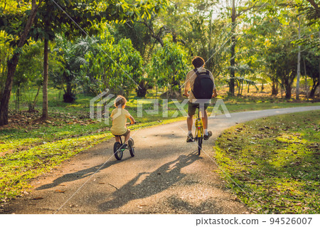 Happy family is riding bikes outdoors and smiling. Father on a bike and son on a balancebike 94526007