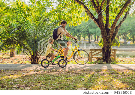 Happy family is riding bikes outdoors and smiling. Father on a bike and son on a balancebike 94526008