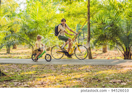 Happy family is riding bikes outdoors and smiling. Father on a bike and son on a balancebike 94526010