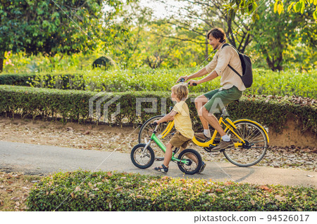 Happy family is riding bikes outdoors and smiling. Father on a bike and son on a balancebike 94526017
