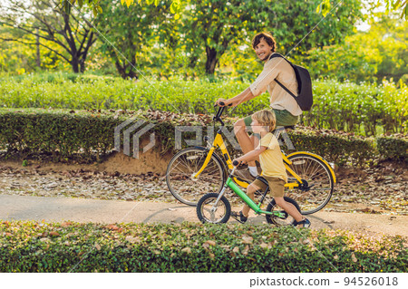 Happy family is riding bikes outdoors and smiling. Father on a bike and son on a balancebike 94526018