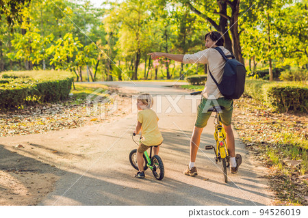 Happy family is riding bikes outdoors and smiling. Father on a bike and son on a balancebike 94526019